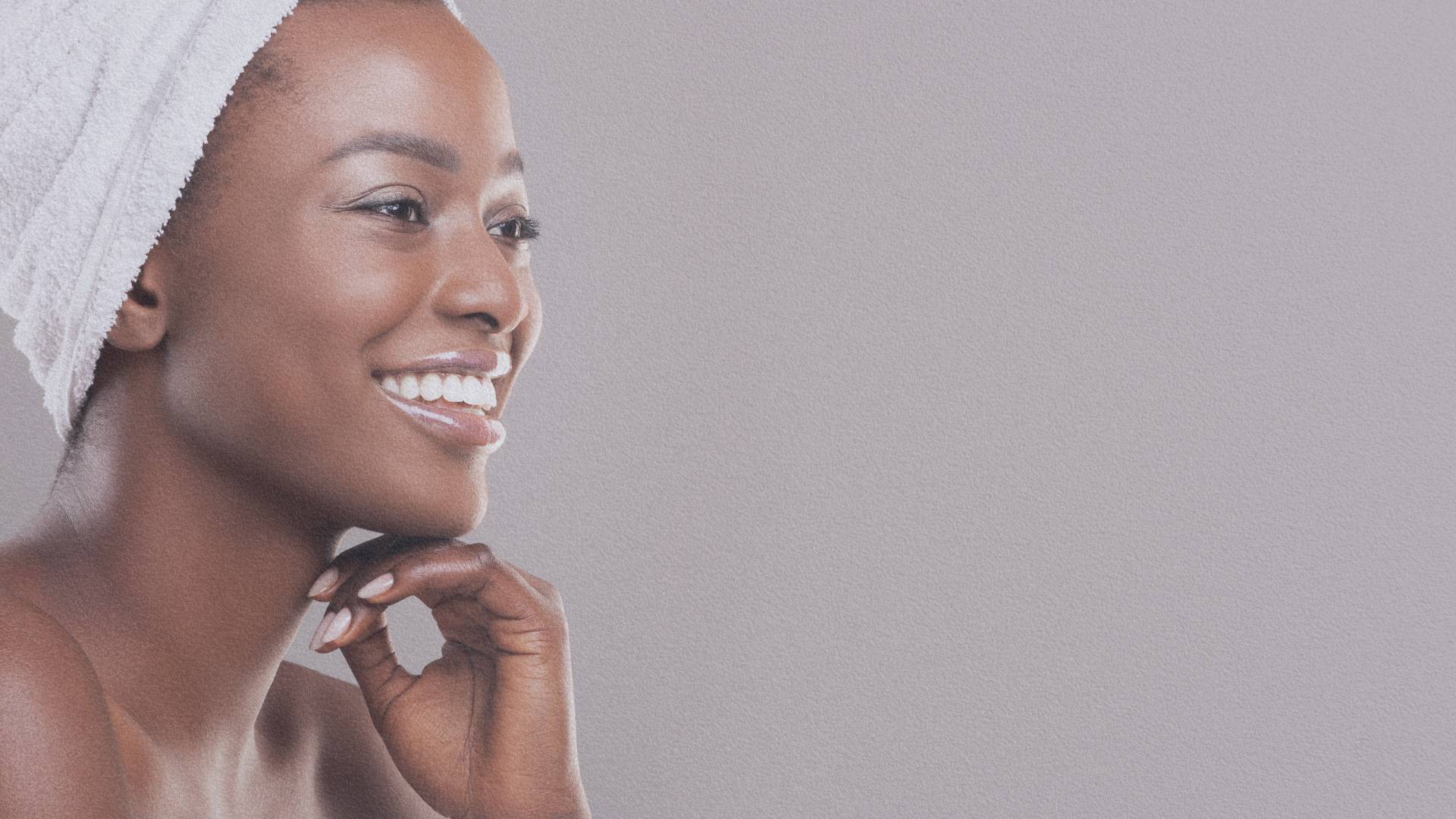 Femme souriante avec une peau éclatante, enveloppée d'une serviette blanche, représentant la beauté naturelle inspirée par le karité