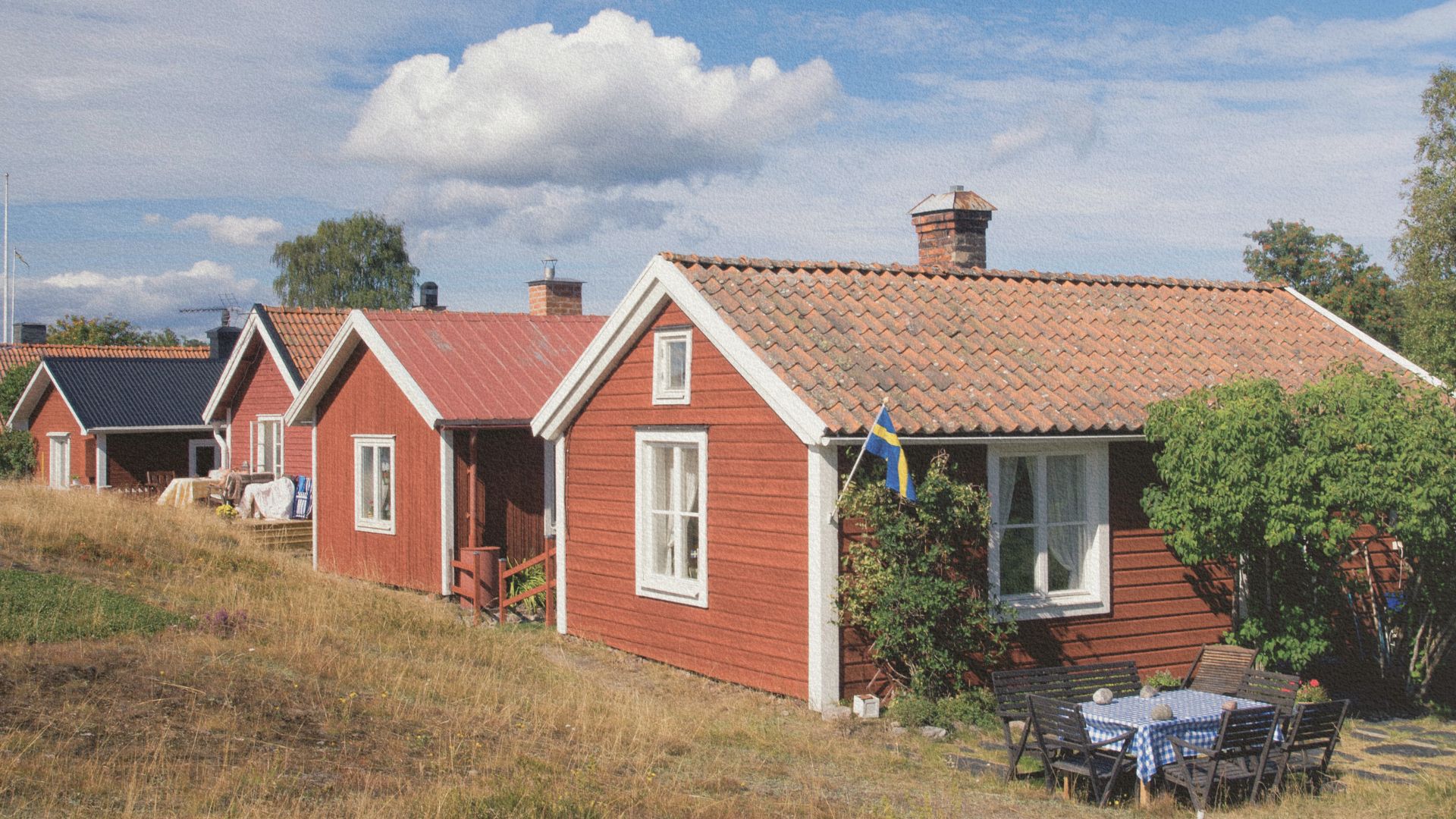 Maisons traditionnelles en bois rouge dans le Hälsingland, avec toits en tuiles, jardin simple et drapeau suédois devant une habitation.