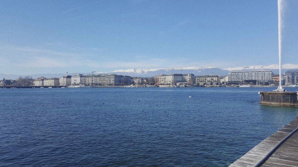 Genève vue depuis le quai, avec le lac Léman, les immeubles de la rive et les montagnes enneigées en arrière-plan