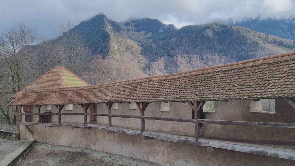 Pont couvert traditionnel à Gruyères avec les montagnes fribourgeoises en arrière-plan, révélant l’implantation du village dans le relief suisse