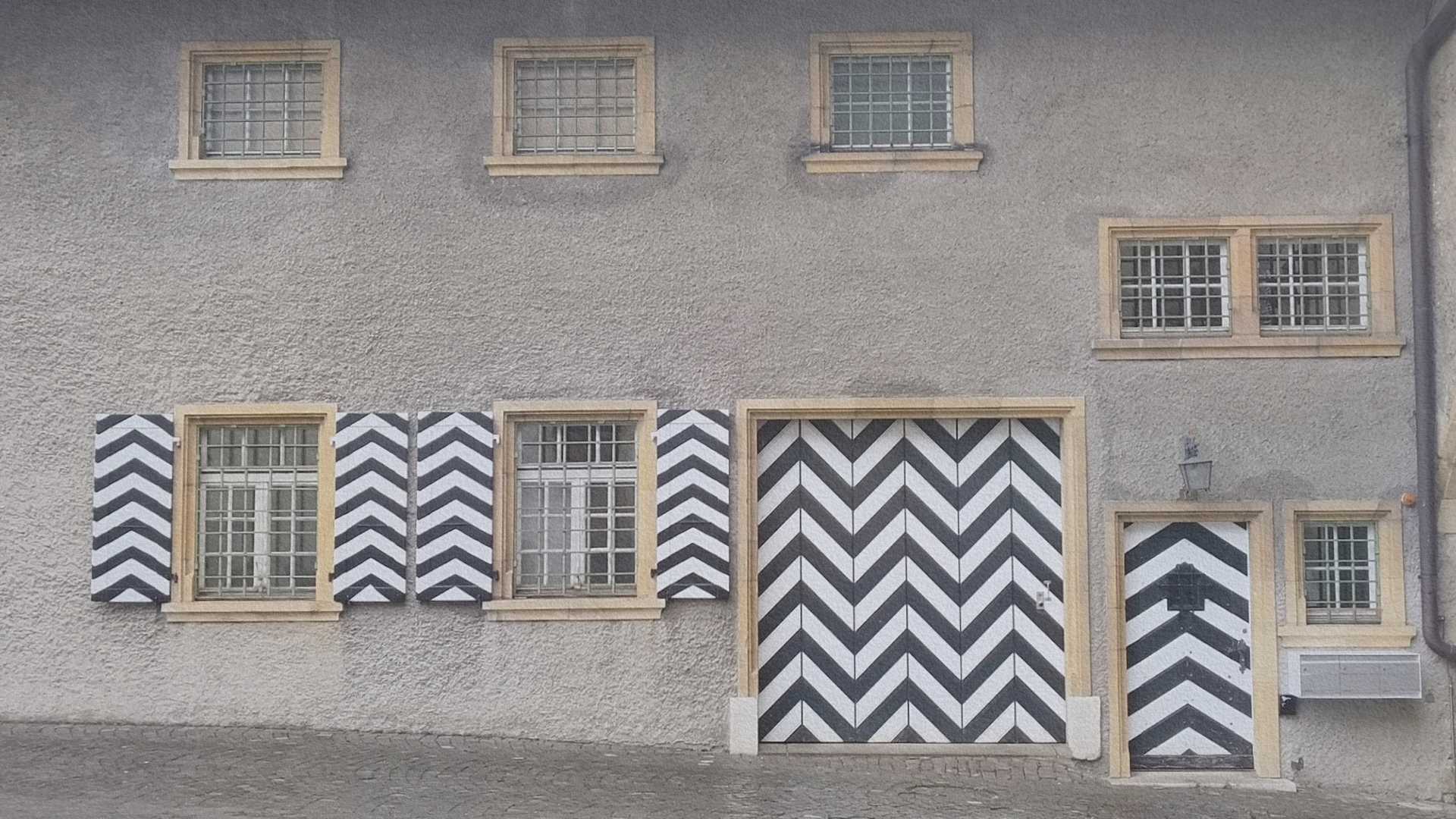 Façade d’un bâtiment historique à Morat avec volets et porte à motif géométrique noir et blanc, architecture caractéristique du centre ancien