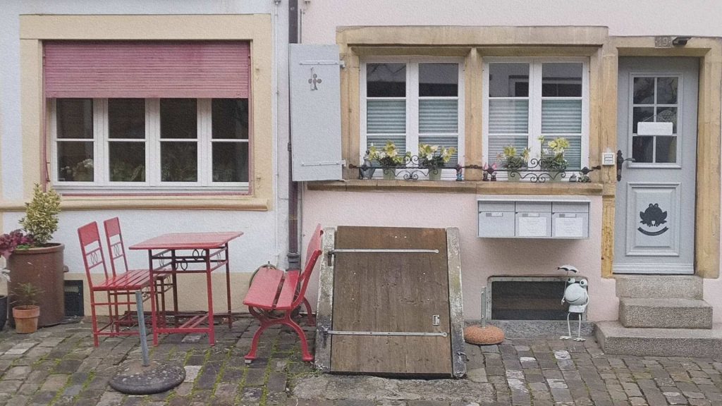 Entrée de maison à Morat avec table et chaises rouges, volets colorés et fenêtres fleuries