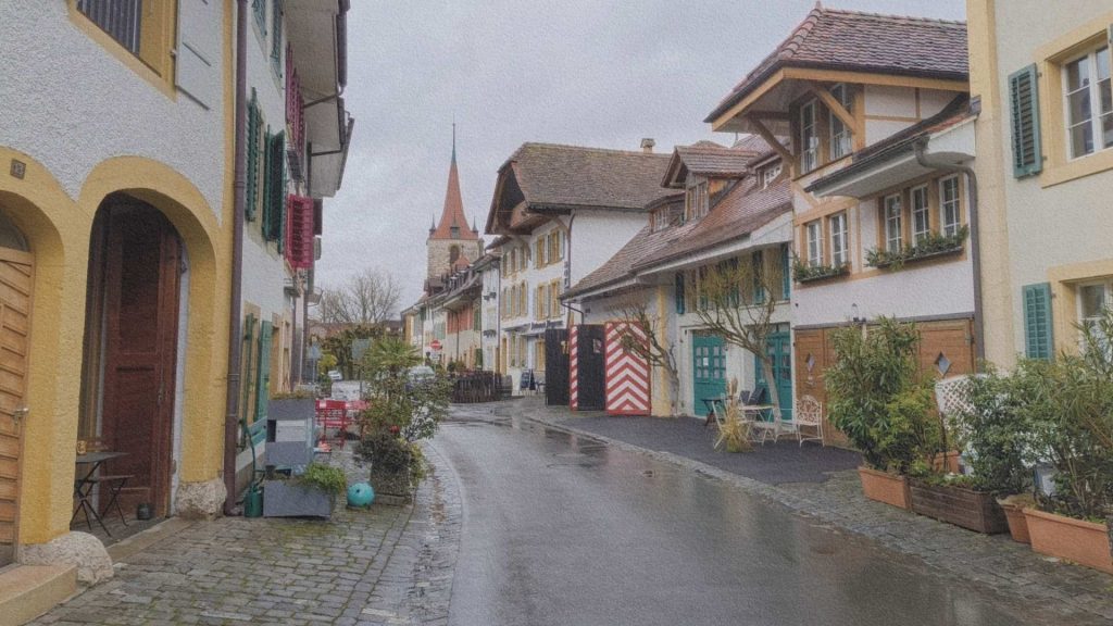Rue du centre historique de Morat en Suisse avec maisons traditionnelles, volets colorés et clocher en arrière-plan