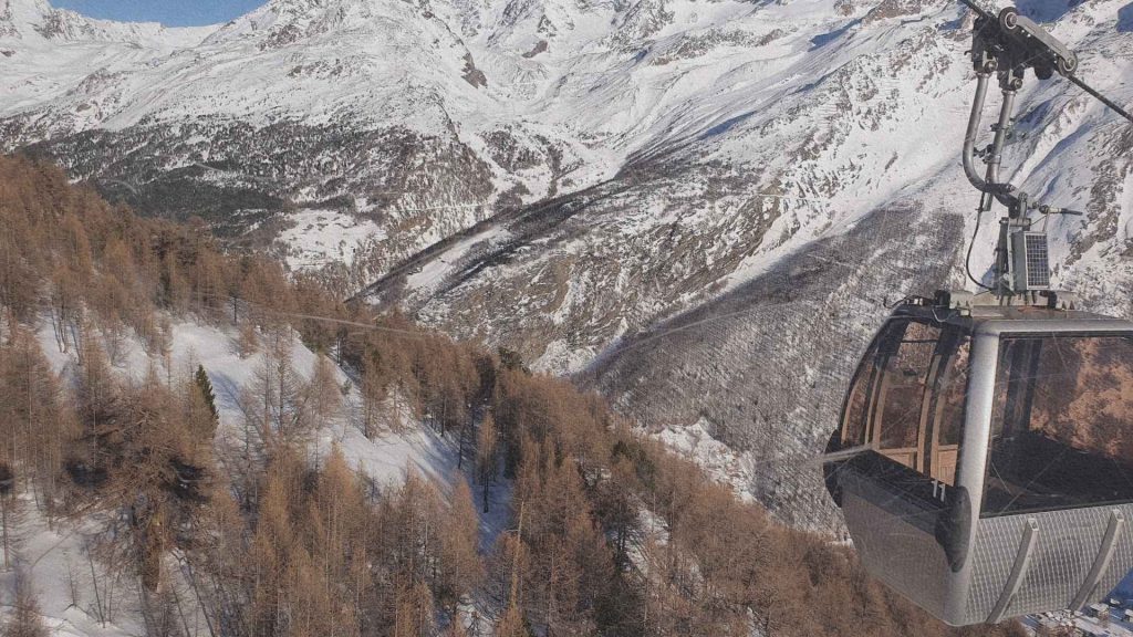 Télécabine surplombant la vallée enneigée de Saas-Fee avec forêts de mélèzes et sommets alpins du Valais
