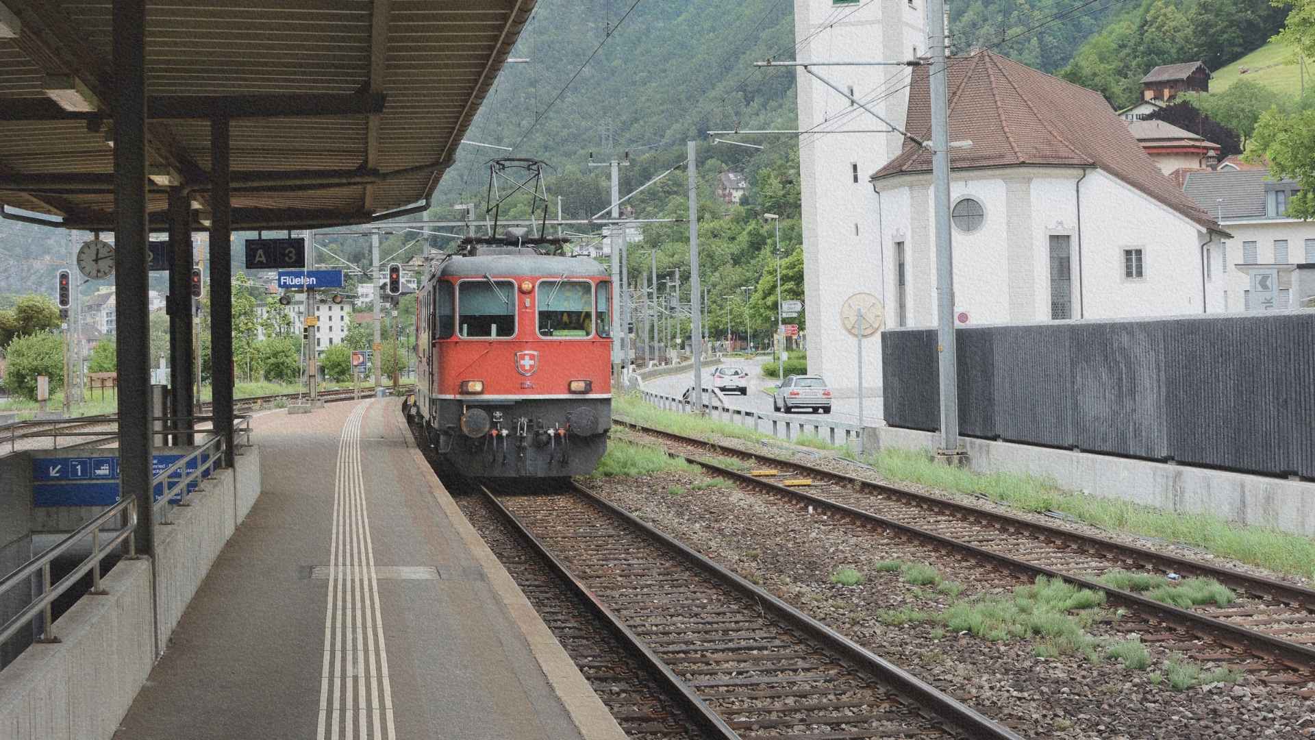 Train rouge des CFF entrant en gare de Flüelen dans une vallée alpine suisse, illustrant l’organisation ferroviaire et territoriale du pays