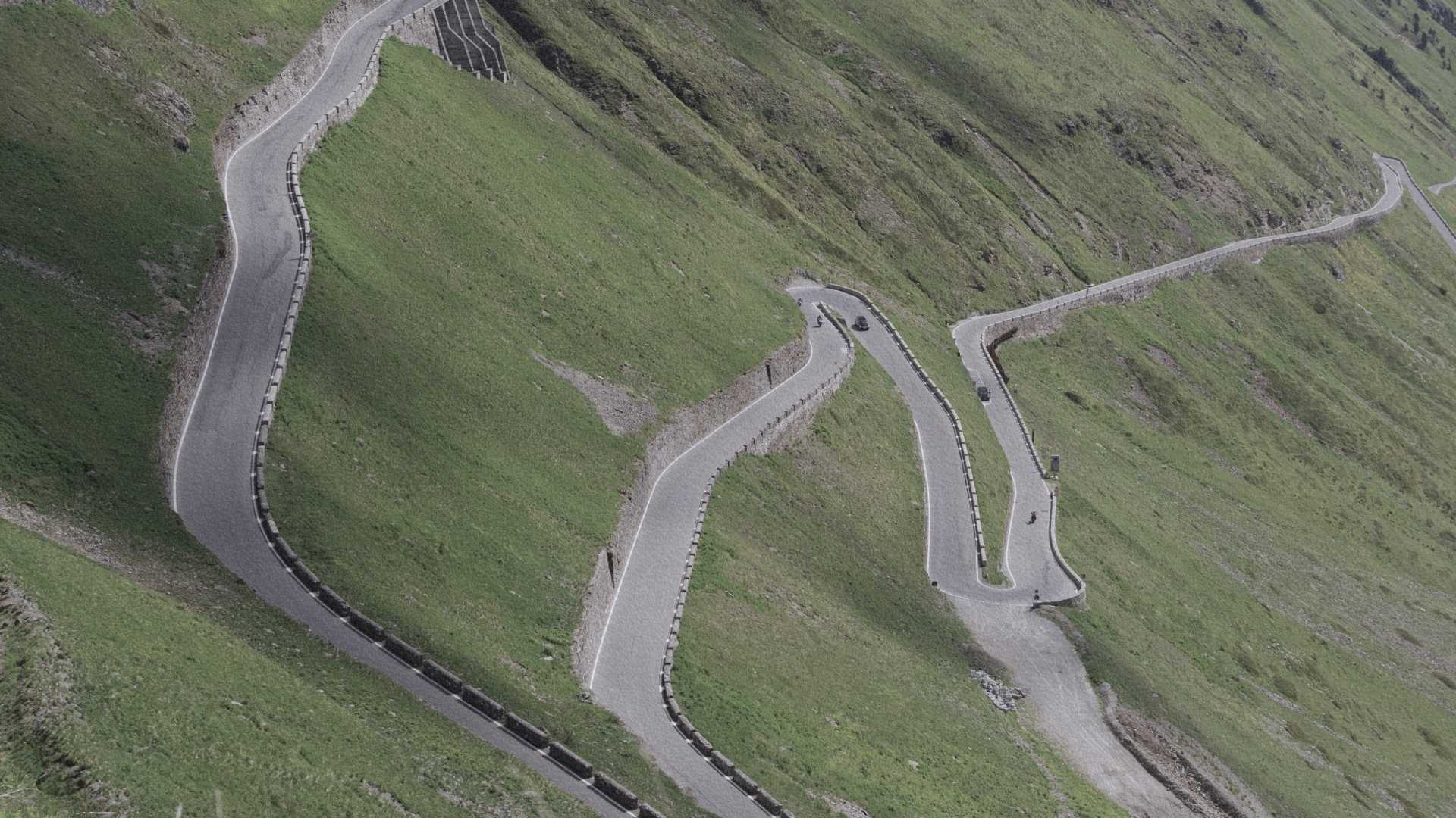 Route en lacets dans les Alpes suisses, serpentant sur un versant herbeux de montagne.