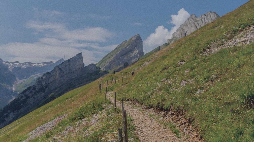 Sentier de randonnée dans le massif de l’Alpstein à Appenzell, longeant une prairie alpine avec vue sur les crêtes rocheuses des Alpes suisses.