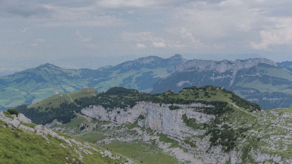 Panorama des falaises calcaires et des reliefs du massif de l’Alpstein à Appenzell, avec sentiers de randonnée et collines verdoyantes des Alpes suisses.
