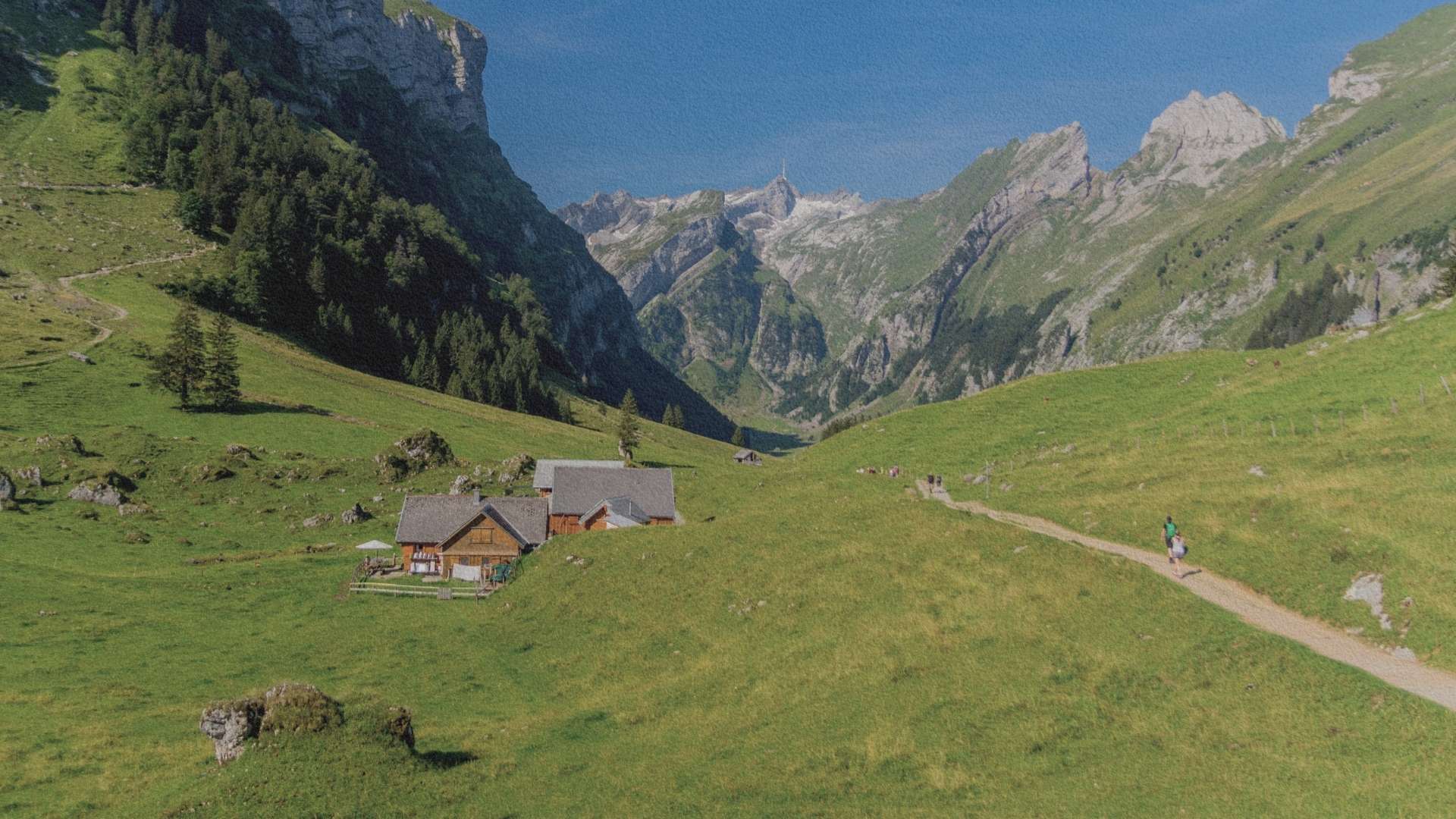 Paysage alpin à Appenzell en Suisse : chalet d’alpage dans une vallée verdoyante entourée de montagnes escarpées et sentier de randonnée traversant les pâturages.