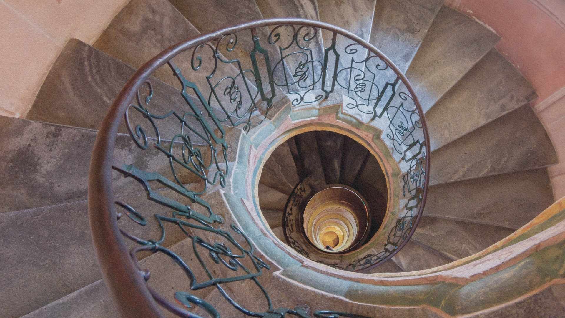 Escalier en colimaçon vu du dessus formant une spirale vertigineuse qui évoque les labyrinthes et les quêtes intellectuelles.