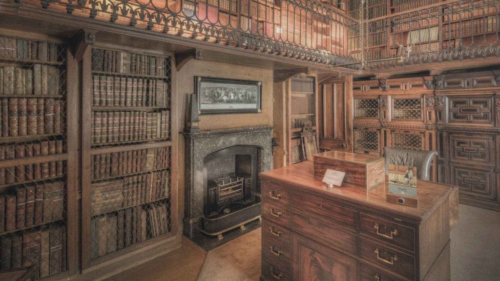 Bibliothèque ancienne aux rayonnages de bois remplis d'ouvrages reliés, avec galerie d'étage et mobilier d'étude évoquant les grands lieux de conservation du savoir.