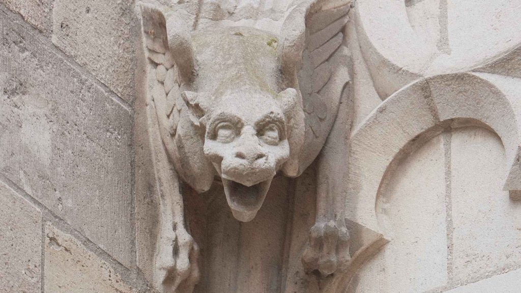 Gargouille sculptée sur une cathédrale médiévale représentant une créature fantastique au visage grimaçant et aux ailes déployées.