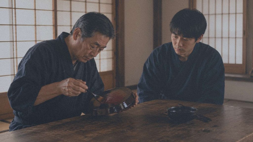 Artisan japonais appliquant une couche de laque sur un objet en bois pendant qu'un apprenti observe silencieusement son geste.