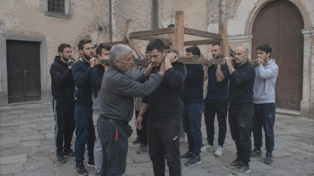Des porteurs italiens répètent le déplacement d’une structure en bois dans une cour.