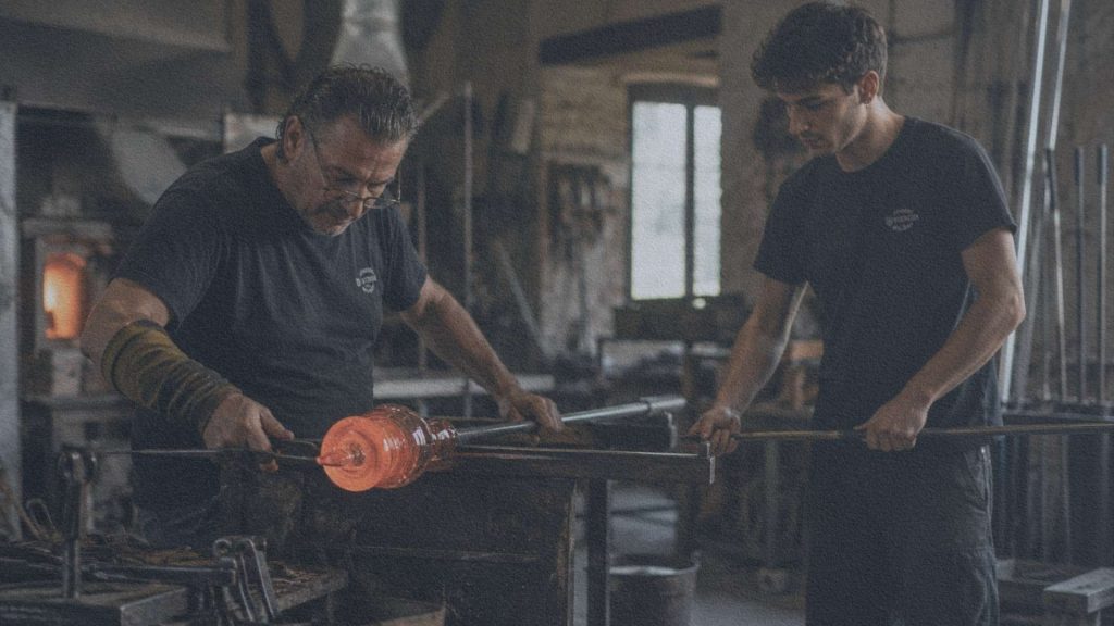 Maître verrier et assistant façonnant ensemble une pièce de verre dans un atelier de Murano.