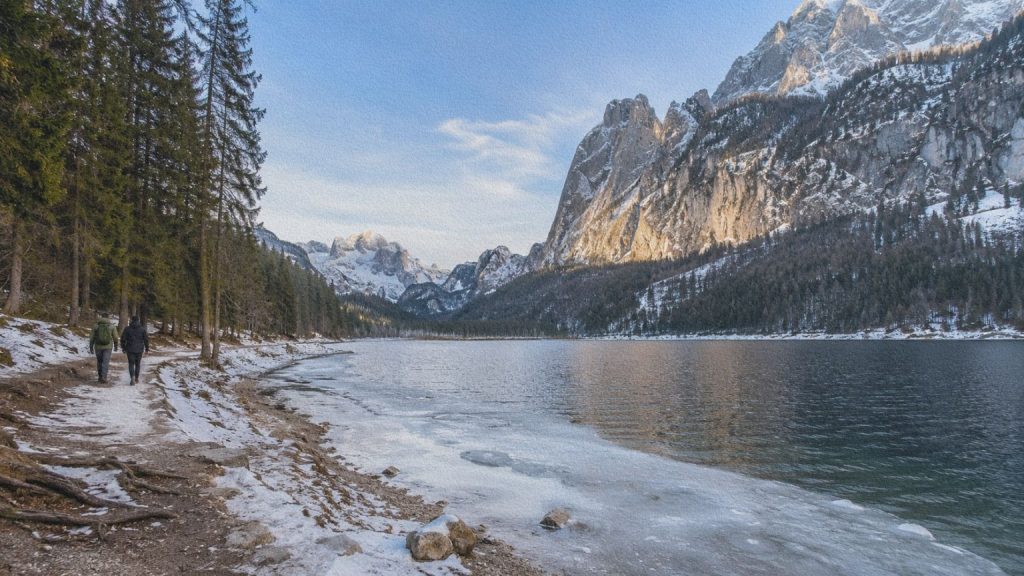 Deux personnes marchant près du Gosausee face au massif du Dachstein pendant l’hiver.