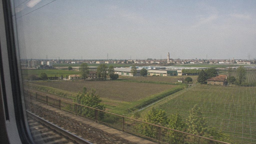 Paysage de la plaine du Pô traversé en train entre terres agricoles, petites villes et activités productives