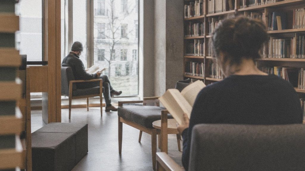 Deux personnes lisent séparément dans le même espace calme d’une bibliothèque.