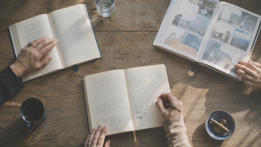 Plusieurs livres de formats différents ouverts autour d’une même table de lecture.